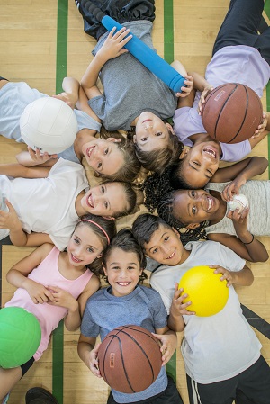 kids laying on gym floor holding different balls