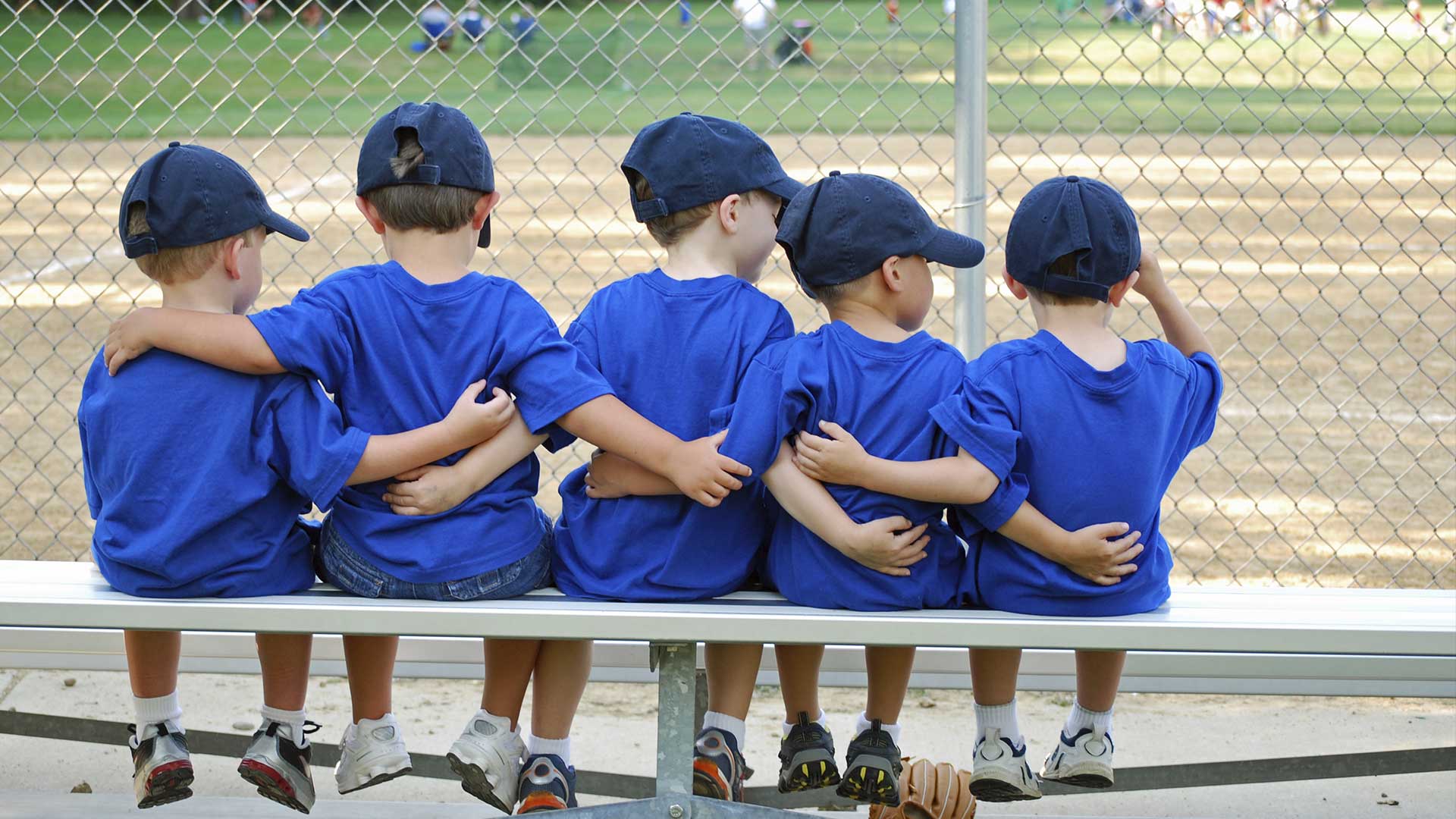 kids sitting on the bench in baseball uniforms